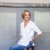 Terri Vinson founder of Synergie Skin in white shirt and jeans looking over her shoulder