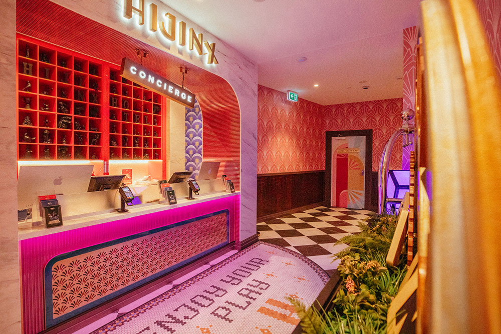 Neon lit reception of Hijinx Hotel with a concierge sign