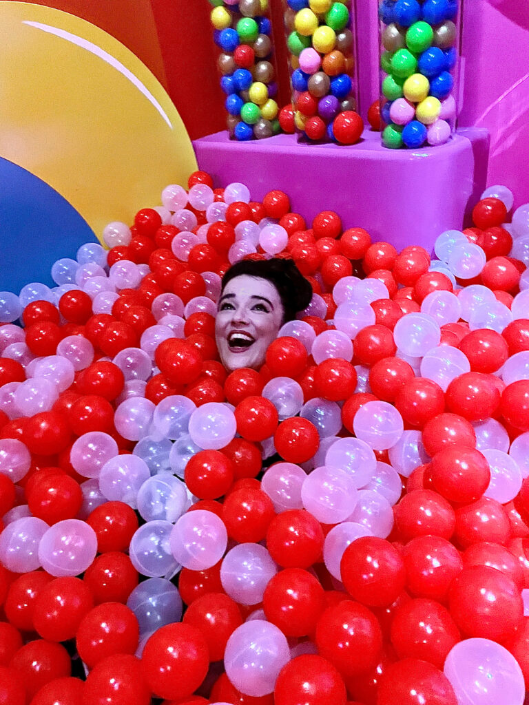 Elizabeth Best, a girl with brown hair completely submerged in a ball pit except for her head. 