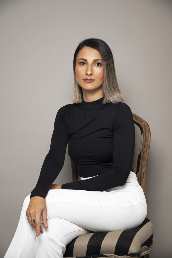 Founder of Mellow Cosmetics, woman with shoulder length balyage hair is posing sitting on a chair.