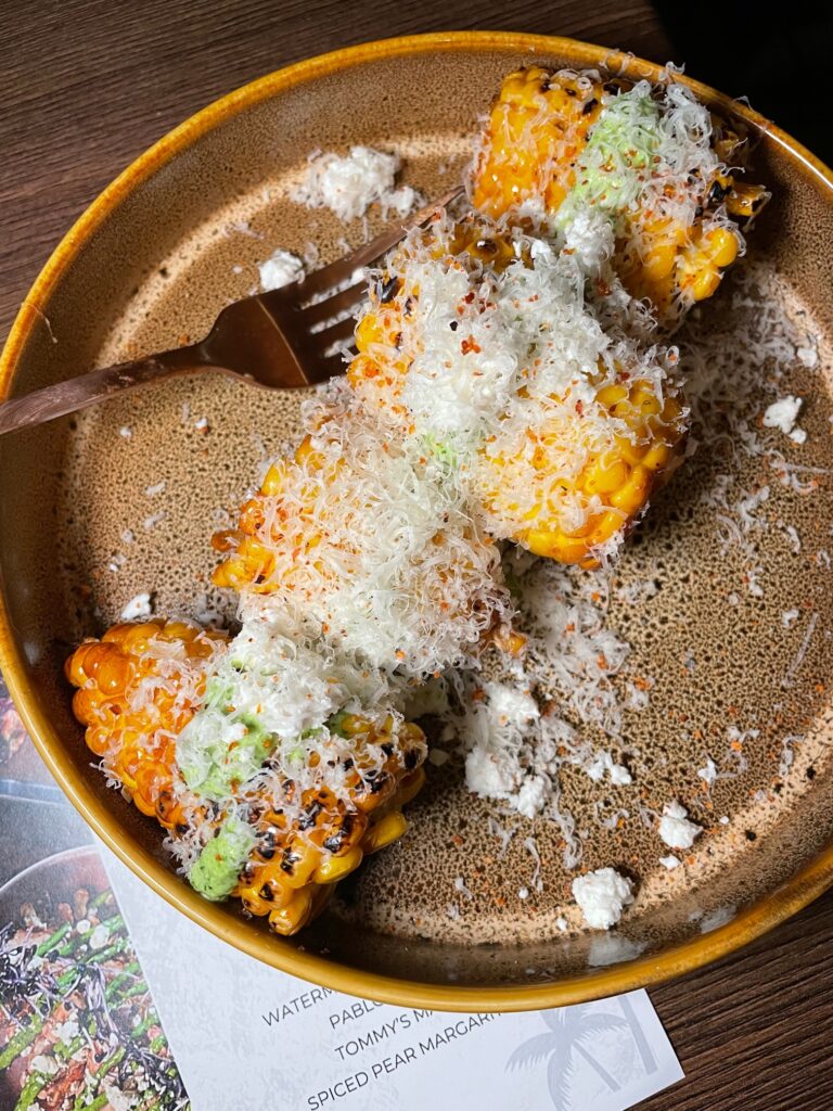 Several cobs of corn on a brown speckled plate covered in grated cheese at Viva La Cali. 