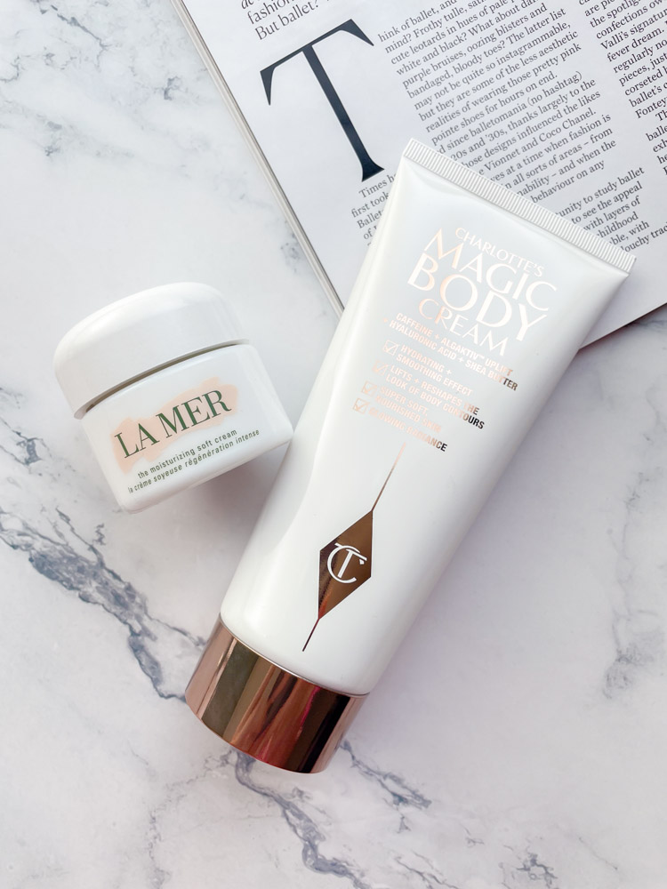 Luxury brands including a La Mer jar and a Charlotte Tilbury Magic Body Cream bottle on a marble background.