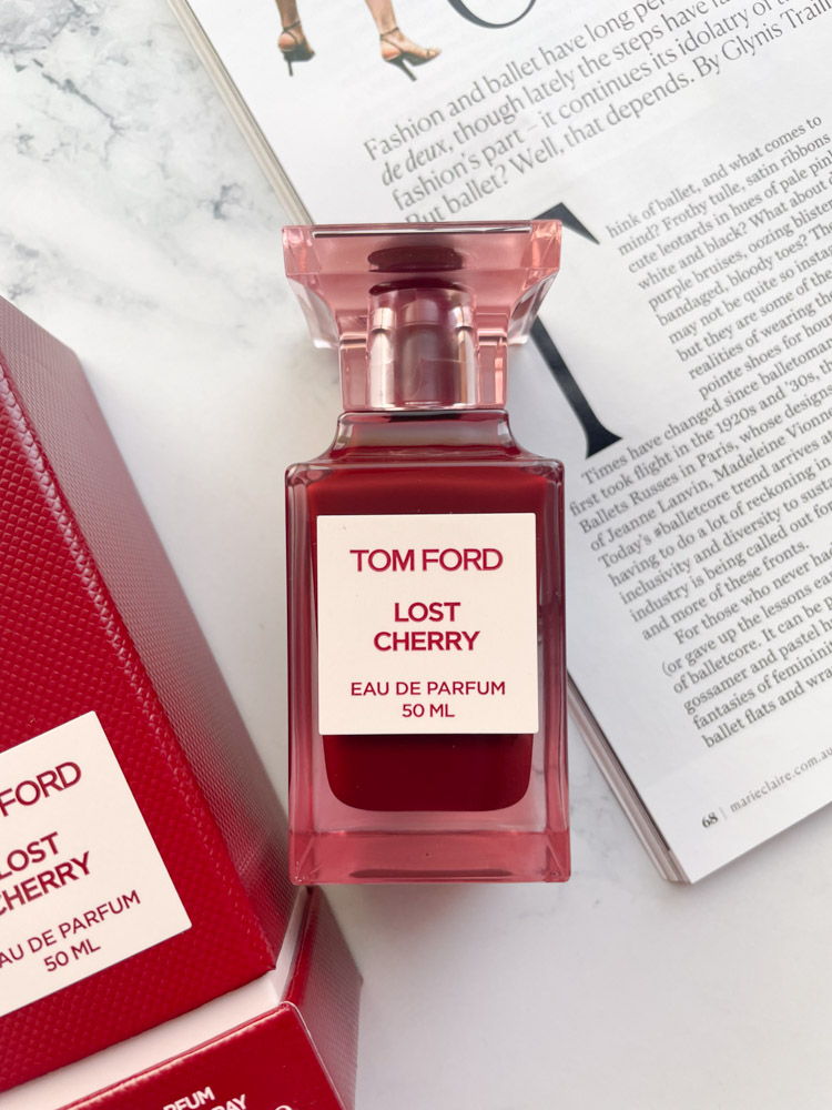 Tom Ford luxury Lost Cherry Eau De Parfum on a marble backdrop with magazine page behind it
