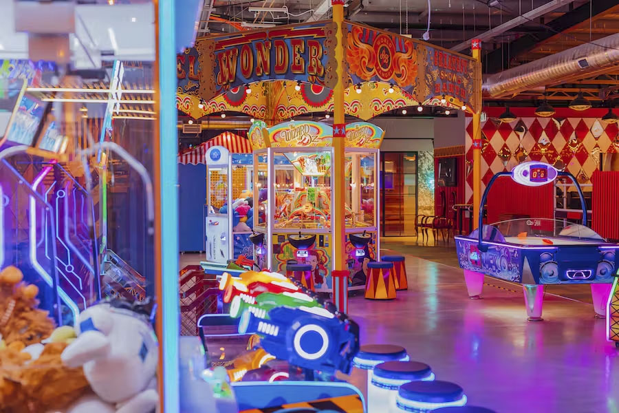 A number of lit up arcade game side by side under a circus themed ceiling. 