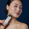Asian woman with rosy cheeks holds CurrentBody Skin Radio Frequency Skin Tightening Device up to the underside of her chin