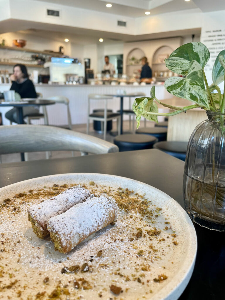 Two small cannoli sitting in the middle of a large plate, with a plant next to it. Sorelle Eatery in the background.