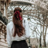 Brunette with long hair and red bow with back to the camera facing the Eiffel Tower in France.