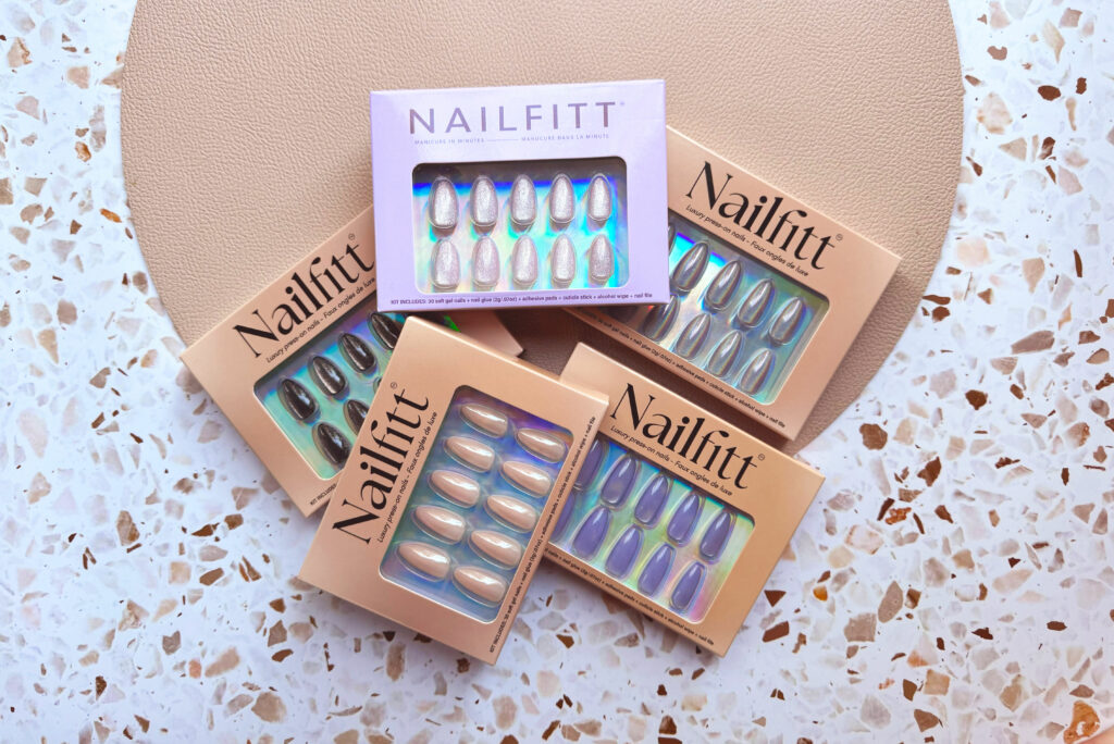 Five pairs of Nailfitt press-on nails in boxes on top of a terazzo counter
