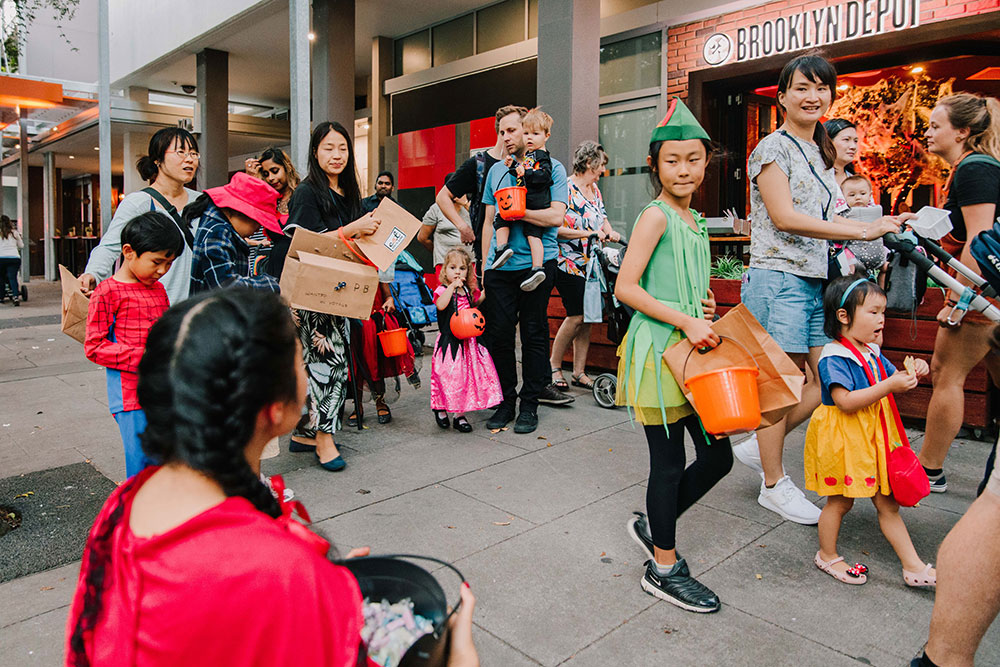 Parents and children in costume trick or treating with pumpkin shaped buckets.