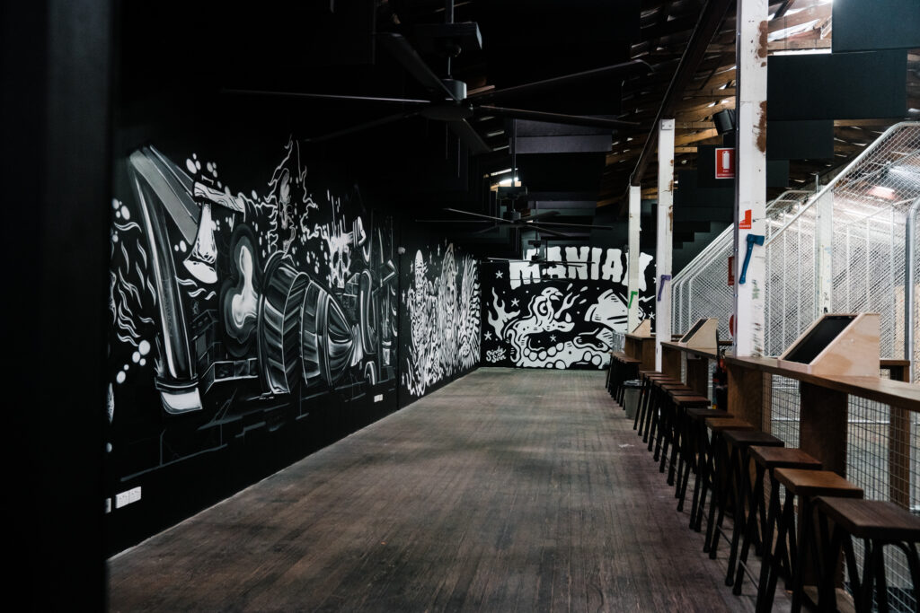 A long room with cages on the right and black and white murals on the left, Maniax written on the wall. 