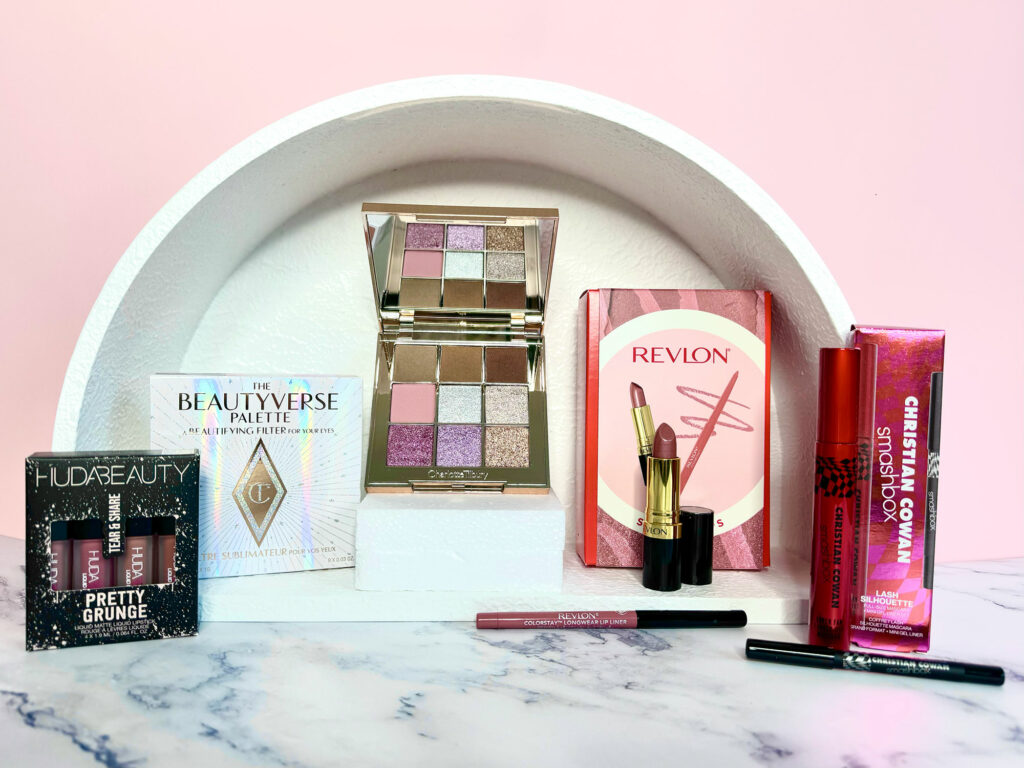 A selection of makeup products in a white arch on a pink background.