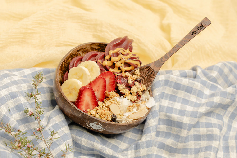 A Yo-Chi branded acai bowl sits on a gingham picnic blanket. 