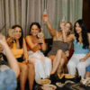 A group of people sitting on a lounge around a coffee table cheersing drinks and smiling