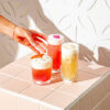 Hand reaching for three rose cocktails on a pink tiled plinth