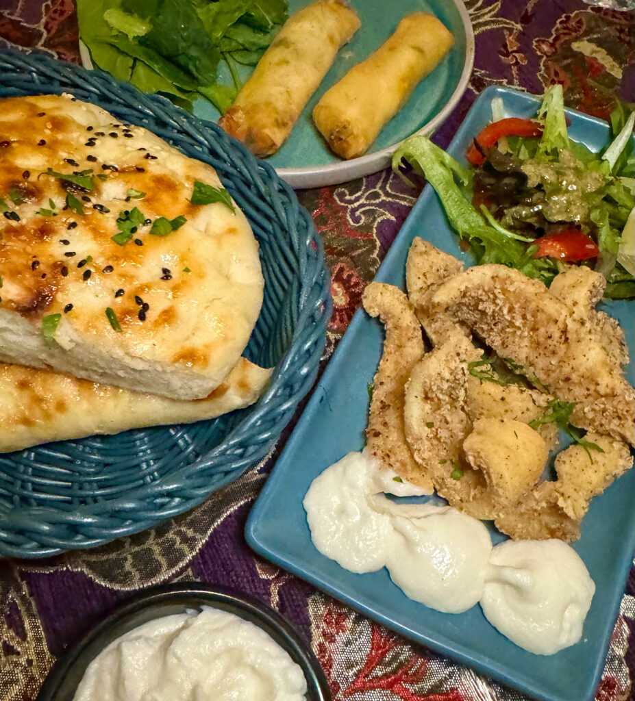 Three plates from an aerial view, one with Turkish bread, one with two spring rolles and one with calamari and salad garnish. 