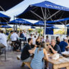 Groups of people sitting at tables under blue Peroni umbrellas