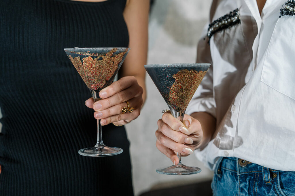 Two people hold cocktails in martini glasses adorened with sparkly glitter. 