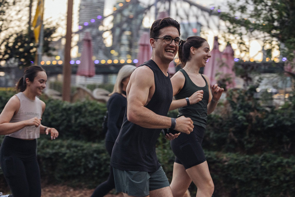 Several people in activewear run past the Story Bridge for Hotel X's Run Club.