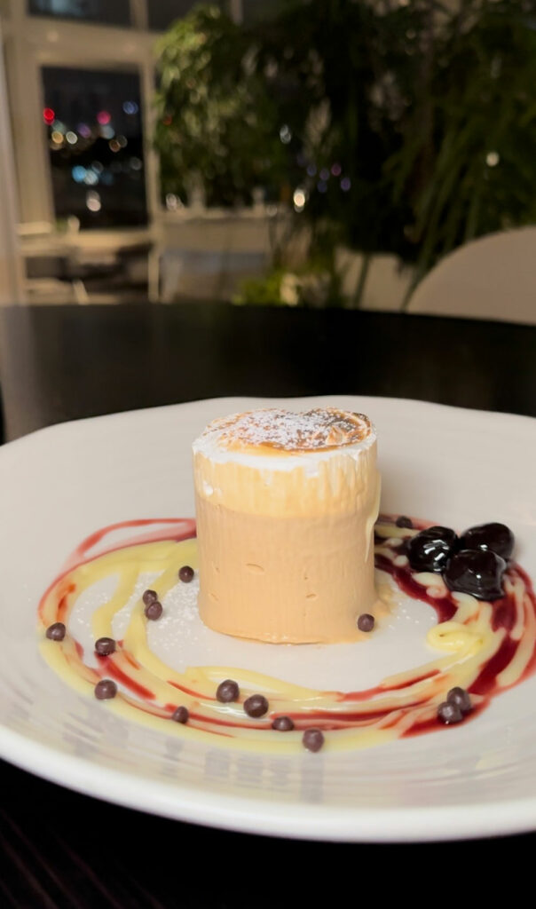 A cappucino parfait. sits on a white plate surrounded by swirls of berry sauce and cream.