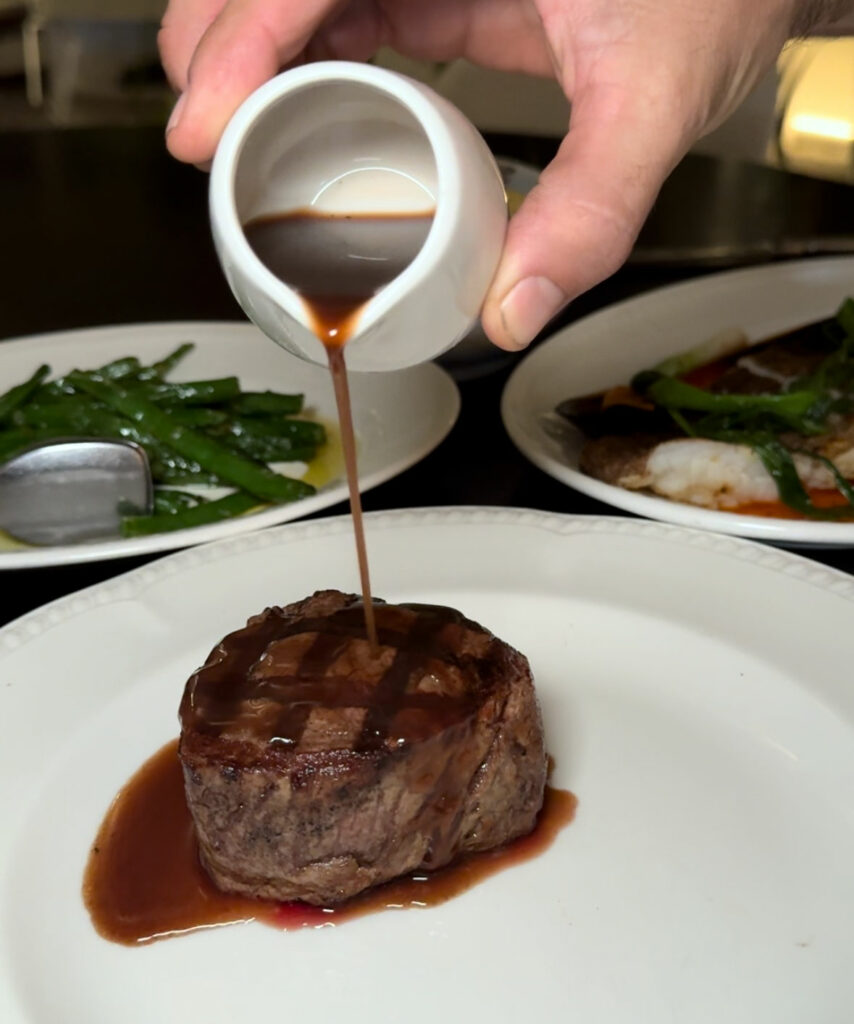 A hand pours beef jus on a 200g eye fillet steak.