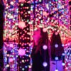 A woman stands in a room covered in colourful lights reflected in infinity mirrors.