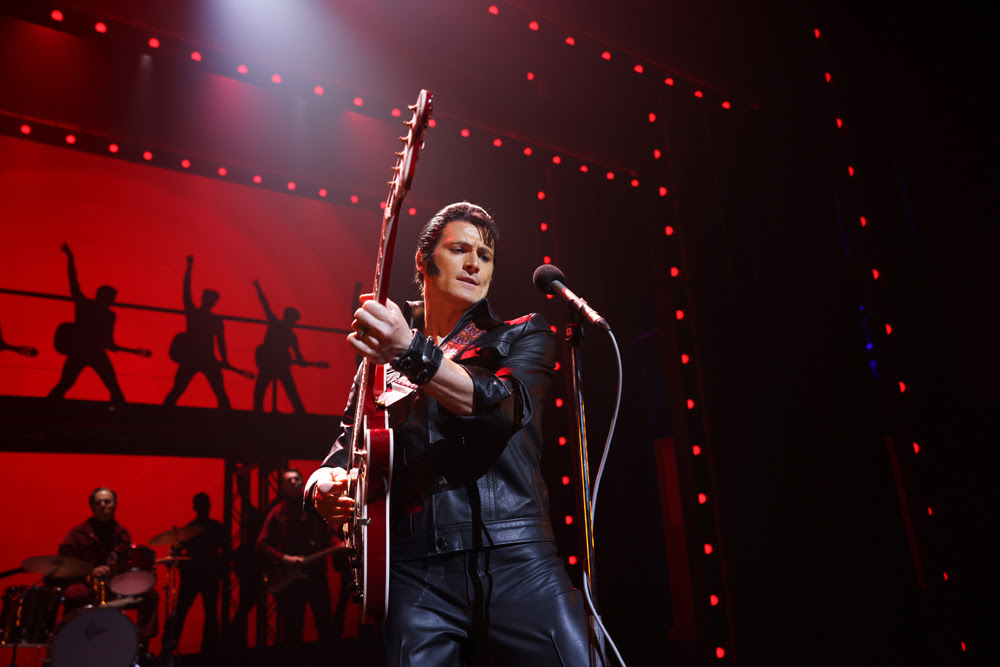 An actor dressed as Elvis plays guitar on a theatre set of Jailhouse Rock