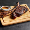 A large tomahawk steak and a gravy boat full of sauce sit on a wooden chopping block.