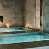 Three pools are lit by candlelight in a room filled with travertine tiles and a fireplace at the end.