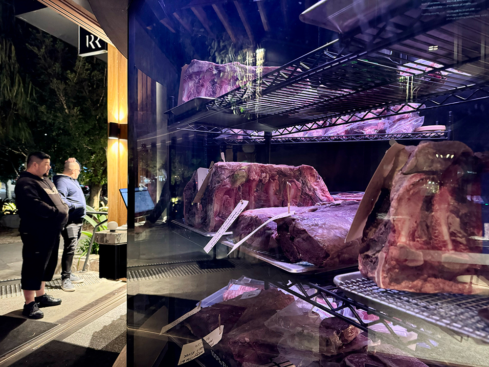 A glass cabinet filled with steak and various cuts of meat as they dry age. 