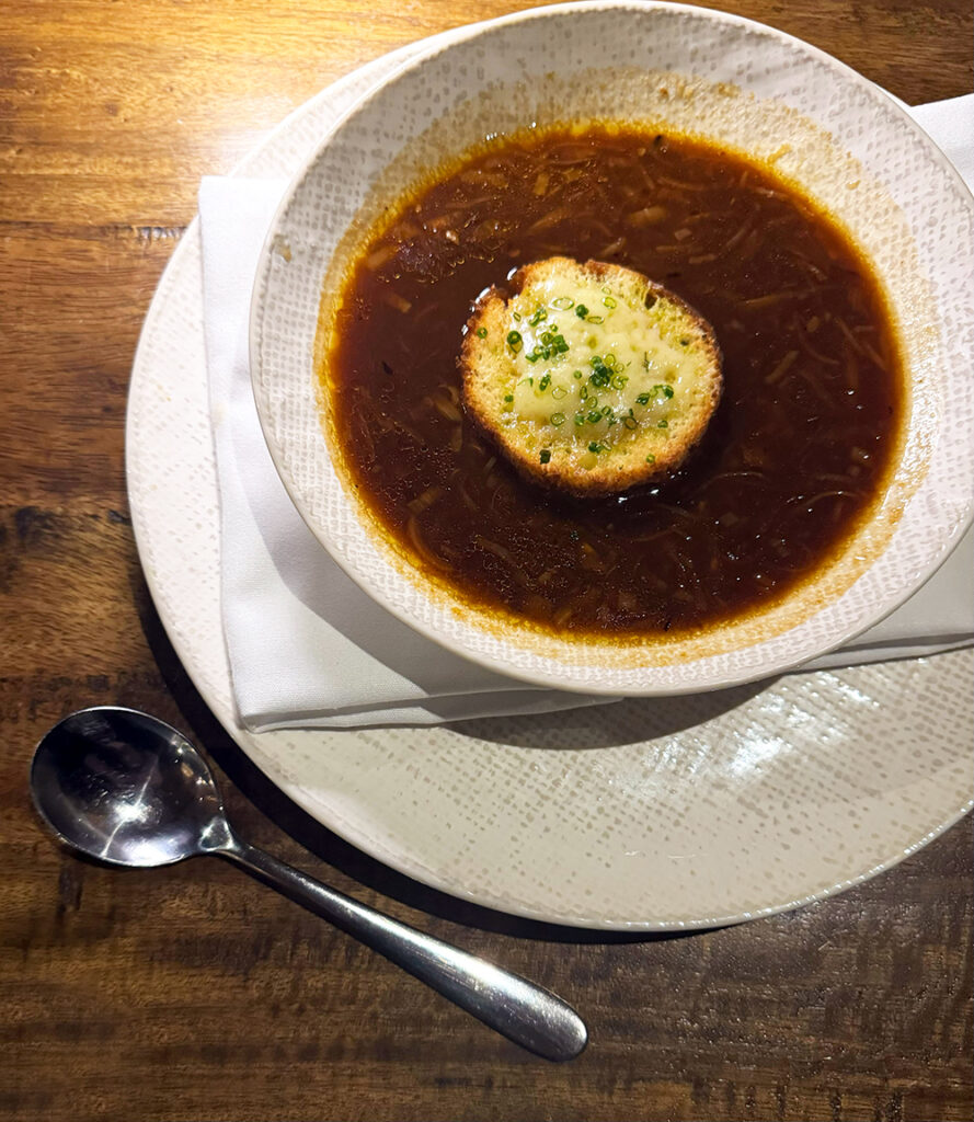 A top down photo of french onion soup with a baguette slice covered in melted cheese on top.