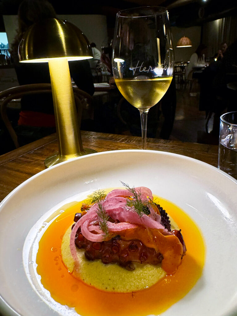 A white plate with orange sauce, yellow polenta and grilled octopus and red onion on top. 