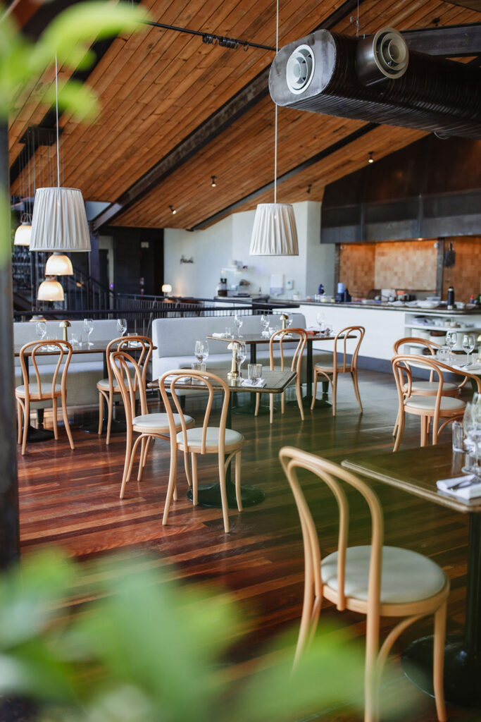 Bentwood chairs and tables on rustic wooden floor in an expansive restaurant with lofted wooden beam ceilings. 