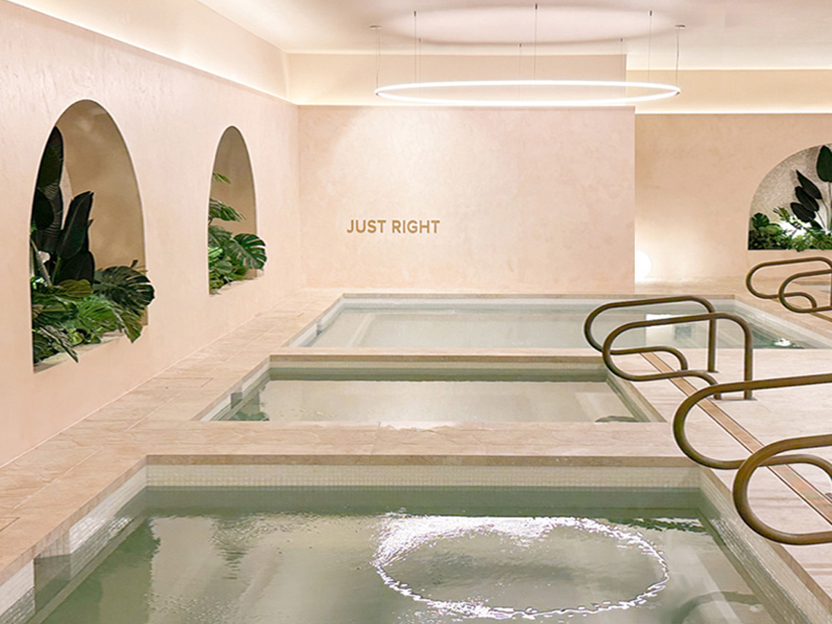 Three heated spas in a row with pinkish sandstone walls and archways with greenery in it.