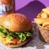 A can of fanta, a burger and a cup of fries sits on a purple background.