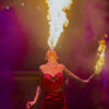 A woman in a red corset breathes fire while holding a lit torch.