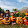 Kids dressed in halloween costumes sit behind a row of carved Halloween pumpkins at south bank