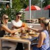 three people sit at a table at Everton Park Hotel with a red umbrella over them, cheersing drinks over a table of food