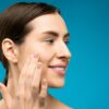 Fresh faced woman smiling while touching face on blue background