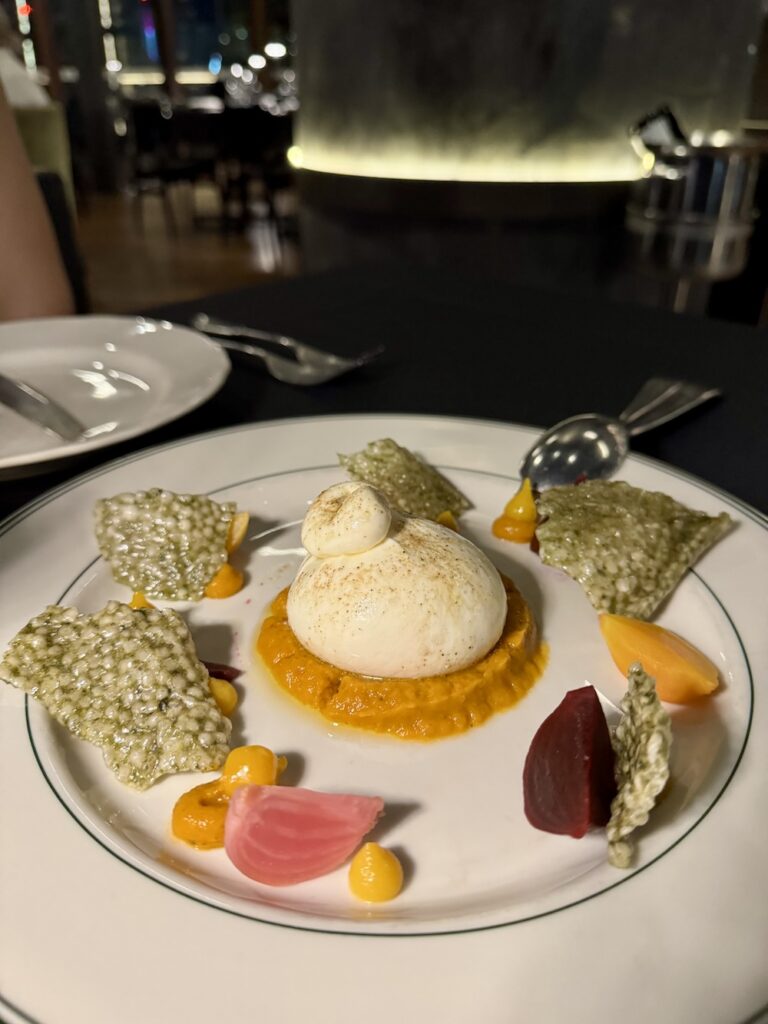 Burrata on a white plate surrounded by beets and tapioca crisps.