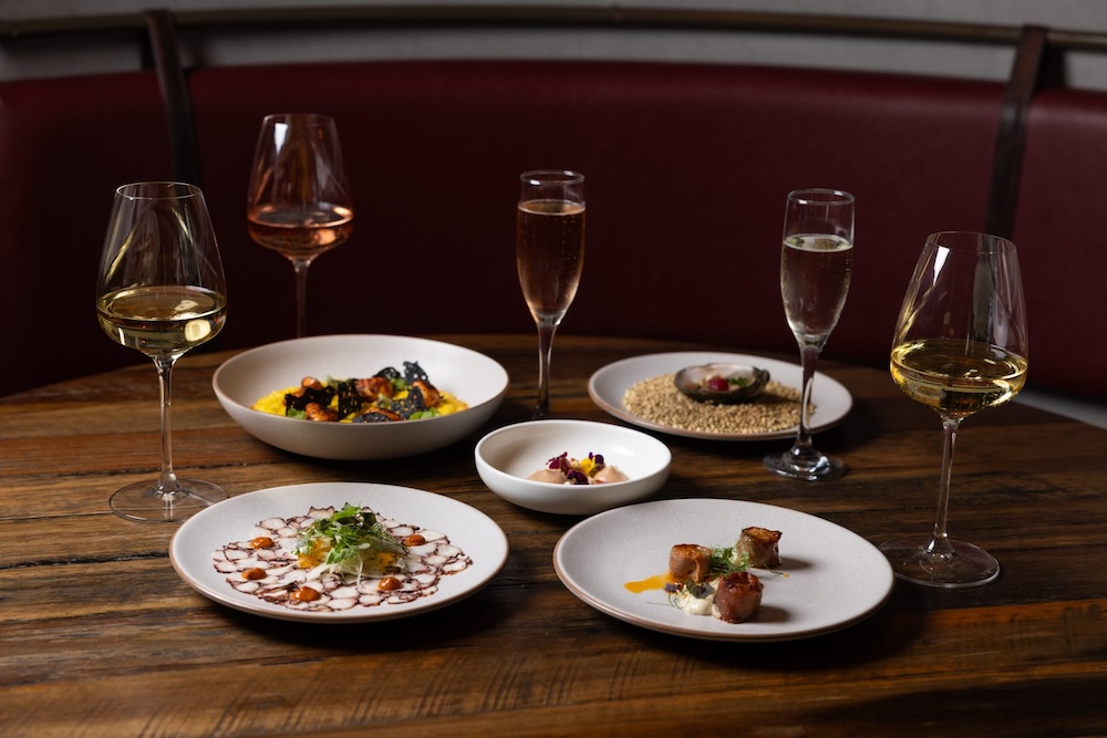 Cálida’s wine and dining events are the hottest ticket in town five seafood dishes on a dark wood table with five glasses of wine at Calida Felix Vasse wine dinner